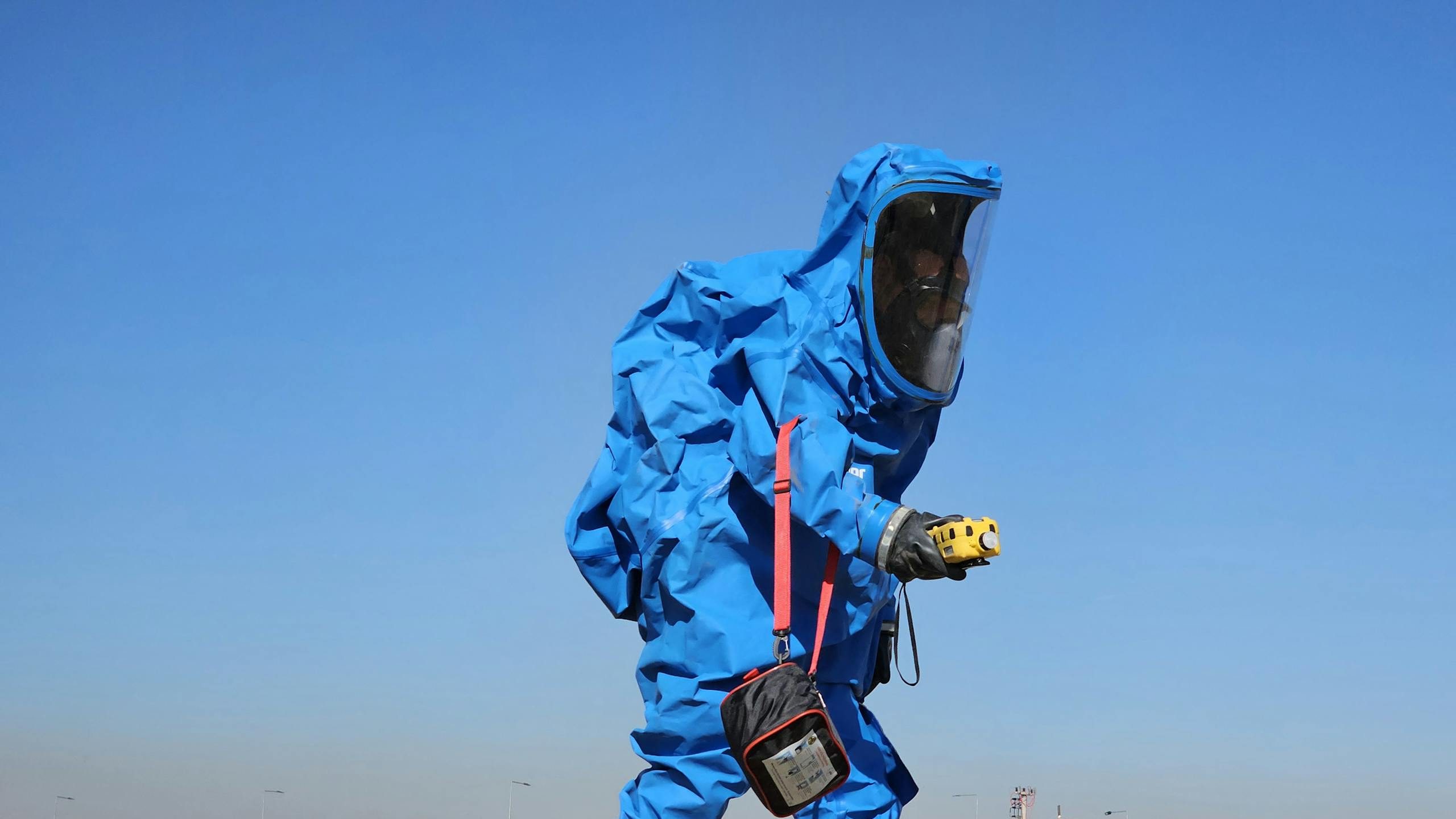 Protective hazmat suit worn by individual inspecting outdoors during daylight.